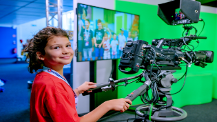 Ein Mädchen bedient eine ORF-Fernsehkamera und filmt Kinder im Greenscreen.