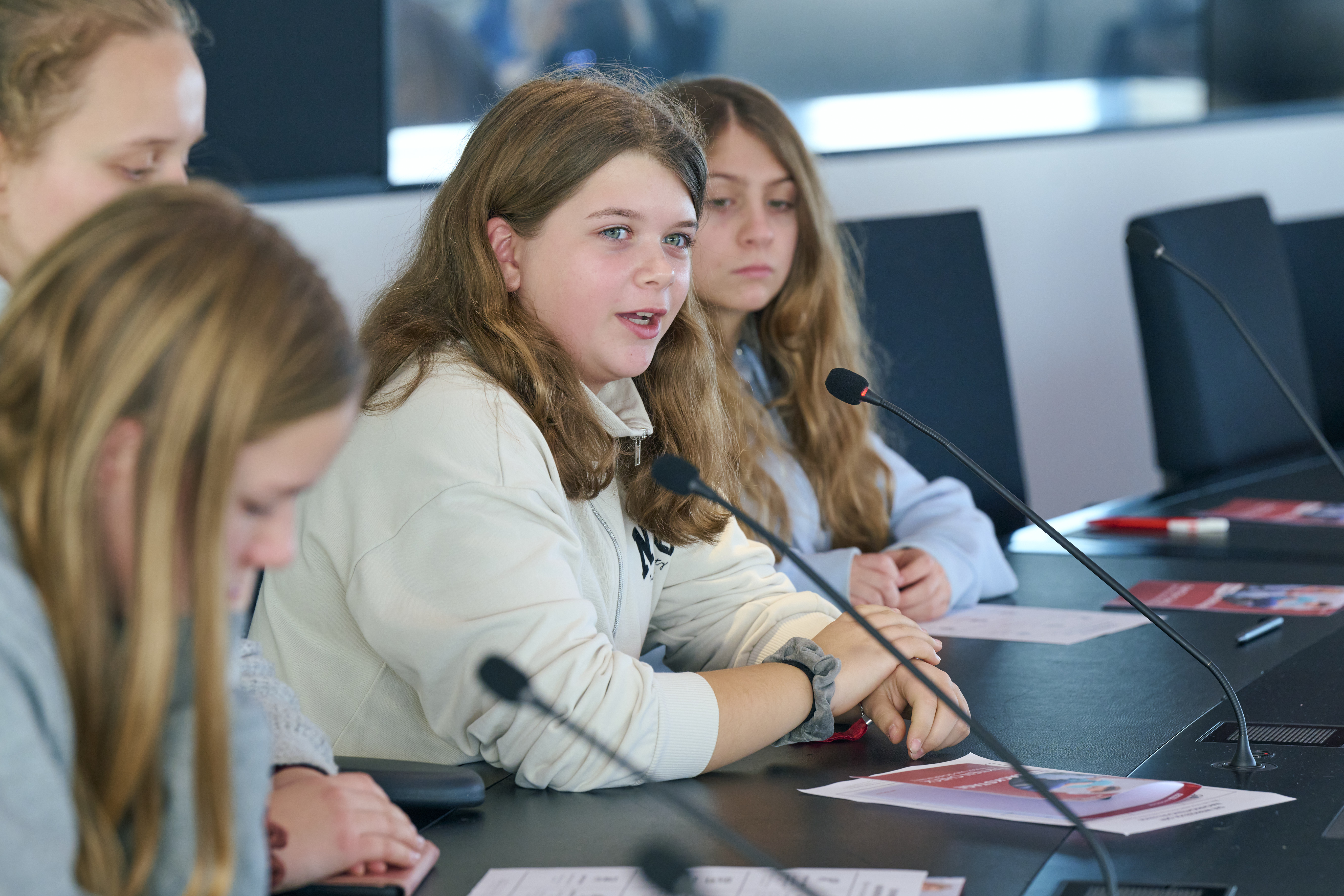 Ein M&auml;dchen sitzt an einem Tisch und stellt eine Frage.