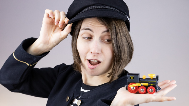 Chrissi Buchmasser mit schwarzer Mütze hält eine kleine Spielzeuglok in der Hand und schaut überrascht darauf.