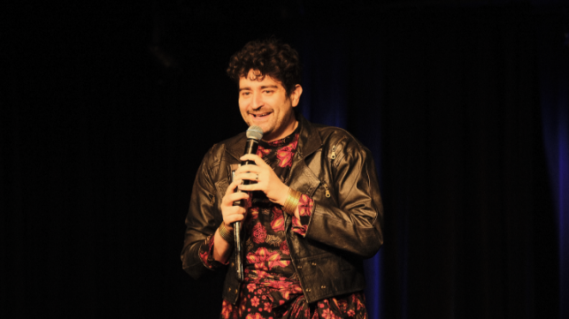 Sebastian Humi steht auf einer Bühne und spricht in ein Mikrofon.