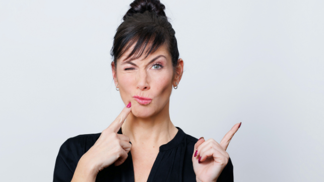 Frau zwinkert und zeigt mit dem Finger zur Seite.