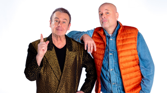 Zwei Männer stehen nebeneinander, einer hebt den Zeigefinger.