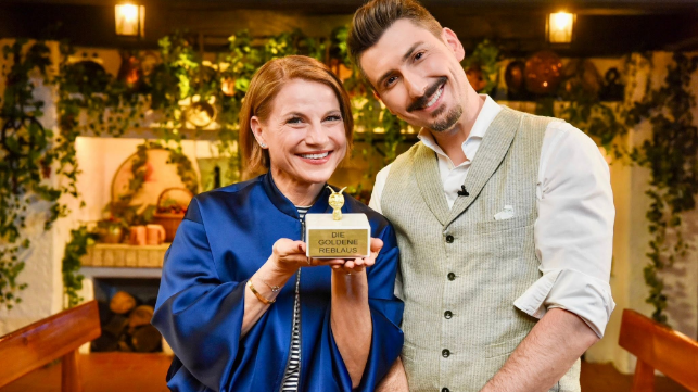 Moderatorin Kristina Sprenger mit einem goldenen Pokal auf dem der Schriftzug "Die goldene Reblaus" eingraviert ist